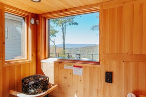 A cabin with a wooden interior, a window with a view of trees and hills, a clock, and a warning sign.