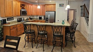 A kitchen with wooden cabinets, a stainless steel refrigerator, a microwave, and a bar area with stools.