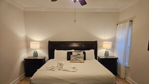 A neatly made bed with a towel and a pillow, two bedside tables with lamps, a ceiling fan, and a window with curtains.