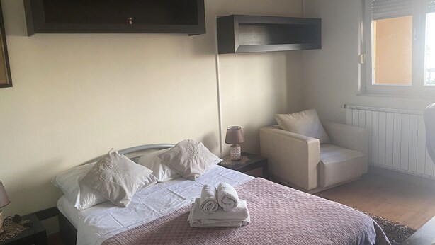 Ein Schlafzimmer mit Bett, Sessel, Nachttisch und Fenster.
