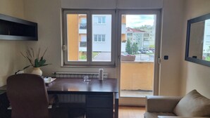 Ein Zimmer mit Esstisch, Stuhl, Sofa, Heizkörper und einem Fenster mit Blick auf Gebäude und eine Straße.