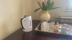 Ein Tisch mit einem Wasserkocher, einem Tablett mit Tassen, einer Zuckerdose und einer Pflanze im Blumenvasen.