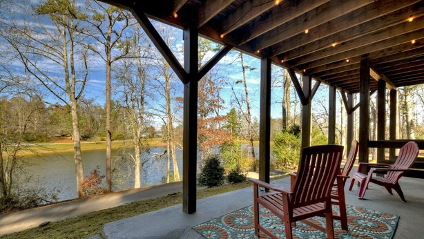 A covered outdoor area with wooden chairs and a patterned rug, overlooking a body of water and trees. - Moon Tower Cabin - Beautiful Water Views, Firepit + More! (Blairsville)