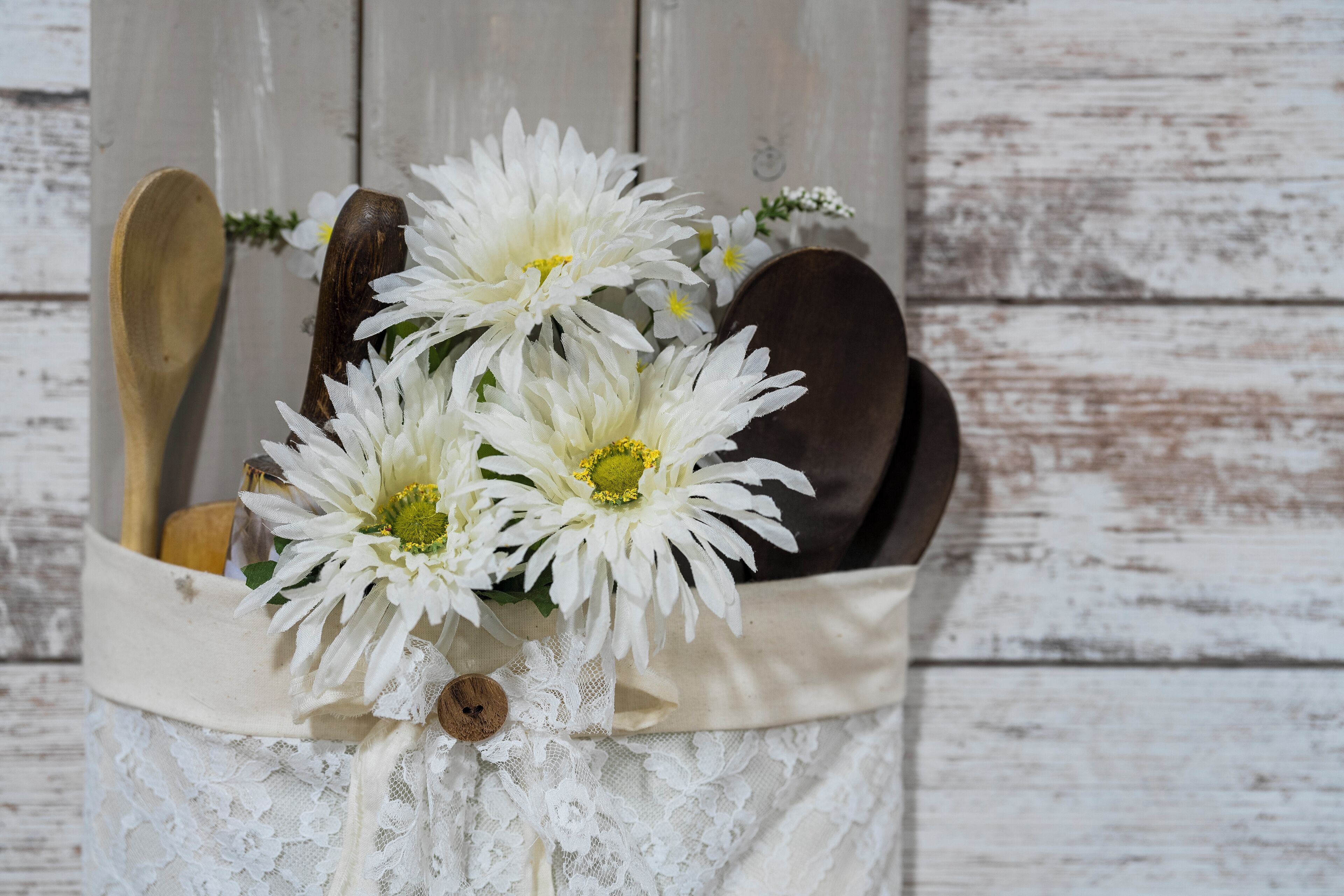 A wooden spoon, a wooden spatula, and a wooden bowl in a white lace bag with white flowers.