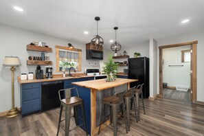 Una cocina moderna con una isla central, taburetes de bar, electrodomésticos integrados y estantes decorativos.