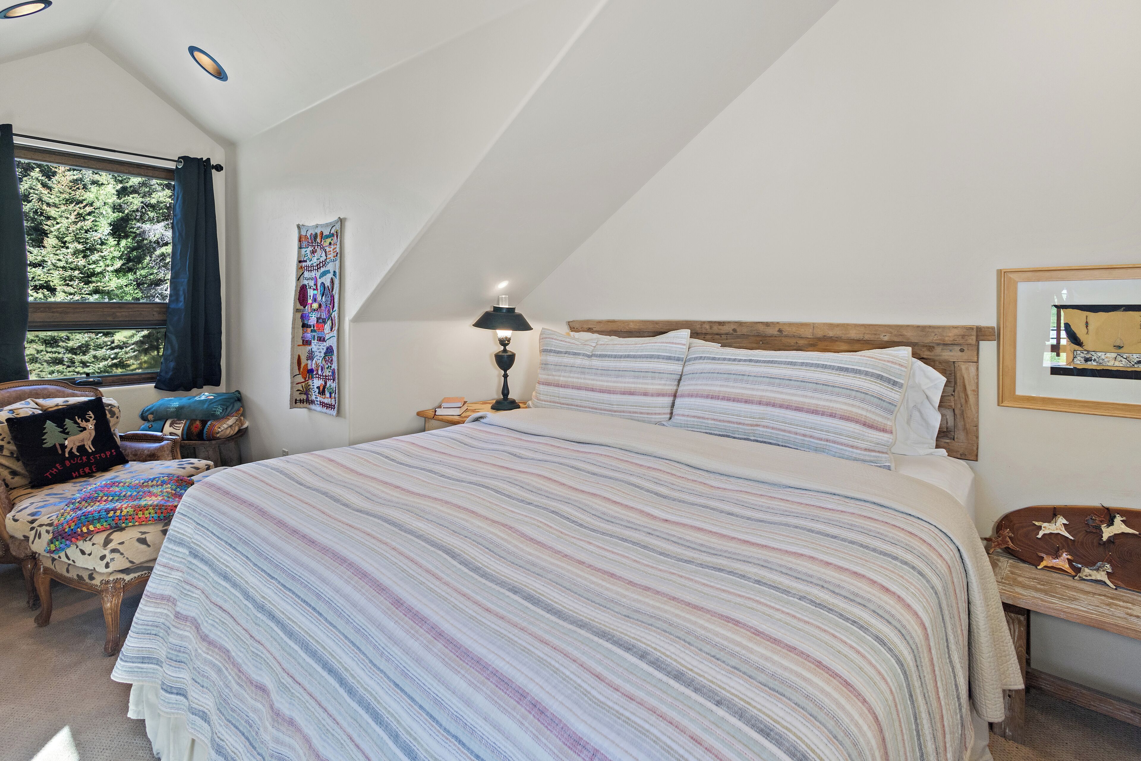 Une chambre à coucher avec un grand lit, une tête de lit en bois, une table de chevet, une lampe, une chaise et une fenêtre avec des rideaux.