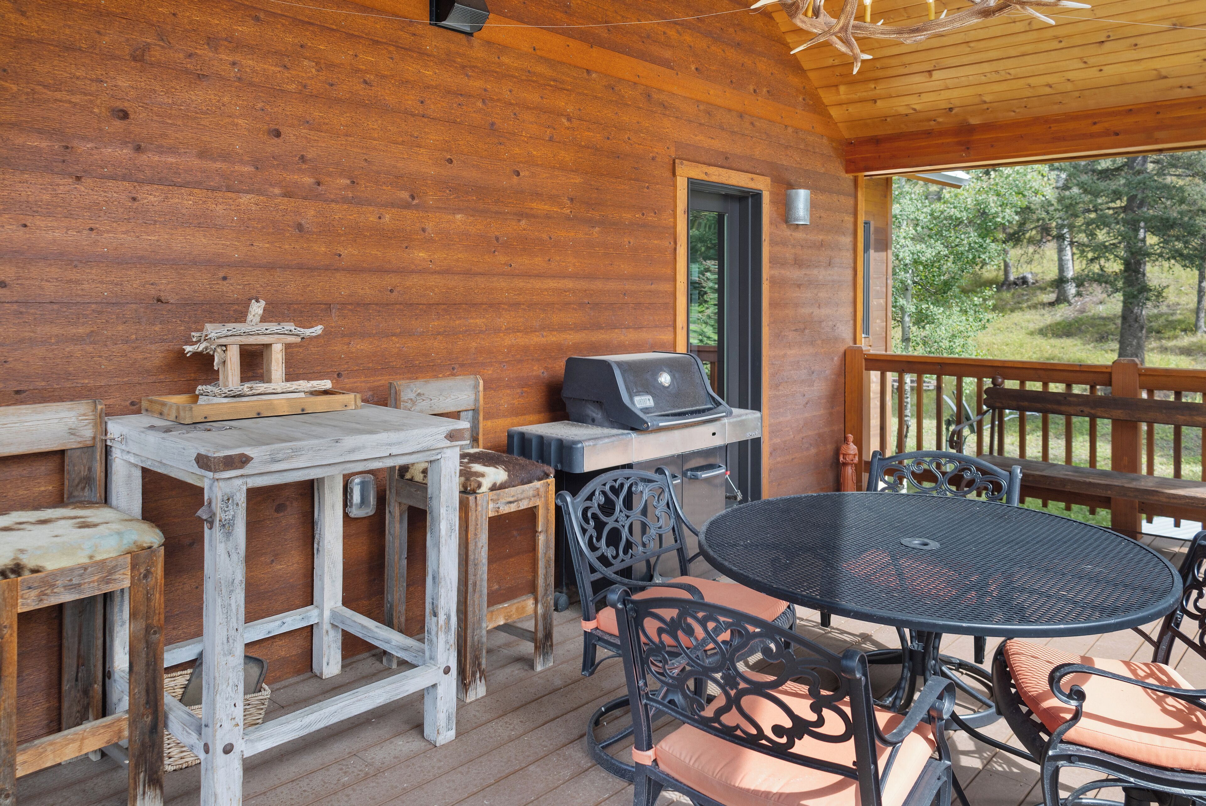 Un patio in legno con un tavolo rotondo e sedie, un barbecue e mobili rustici.