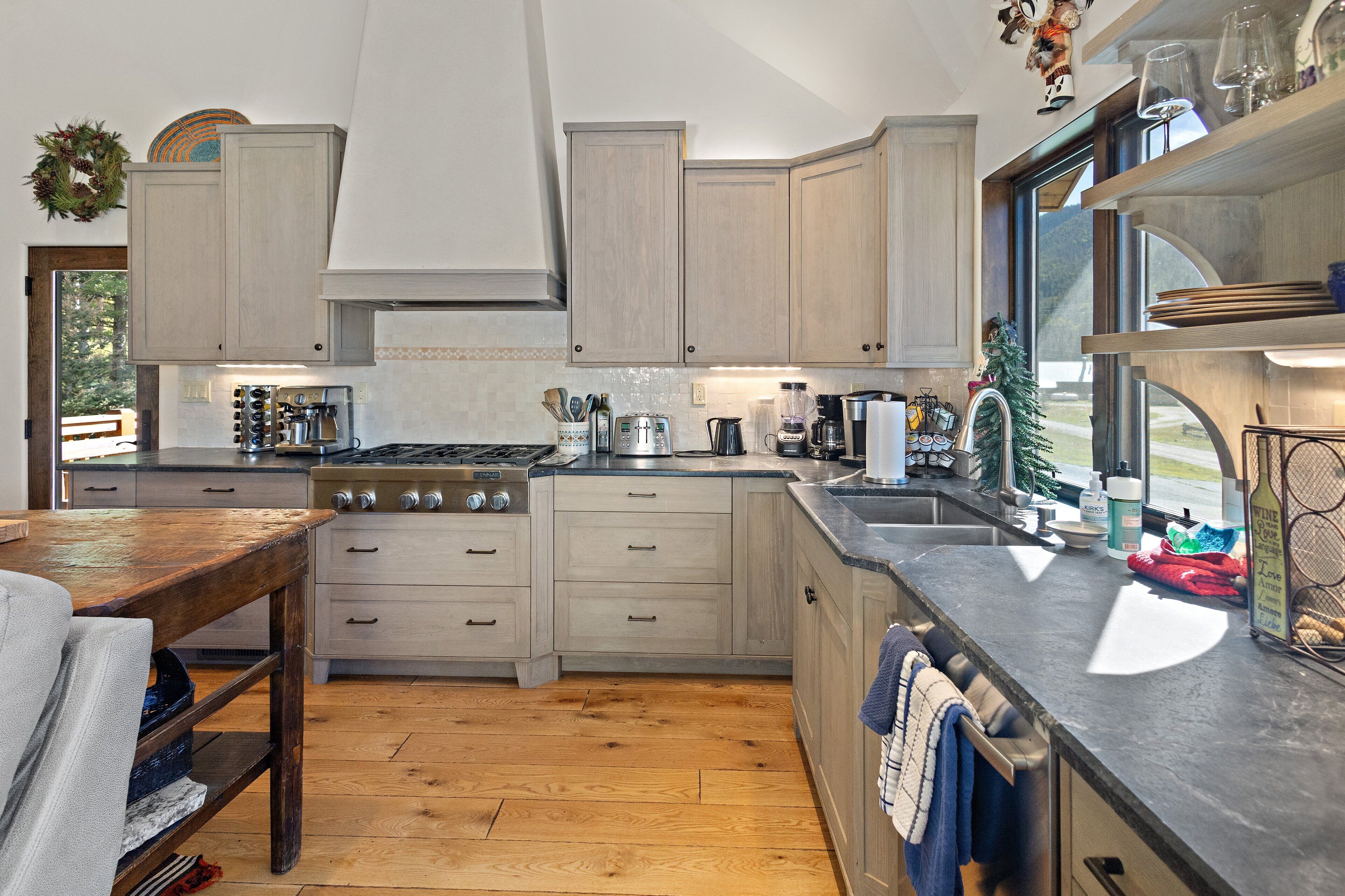 A modern kitchen with wooden cabinets, a large stove, and a window overlooking a scenic view.