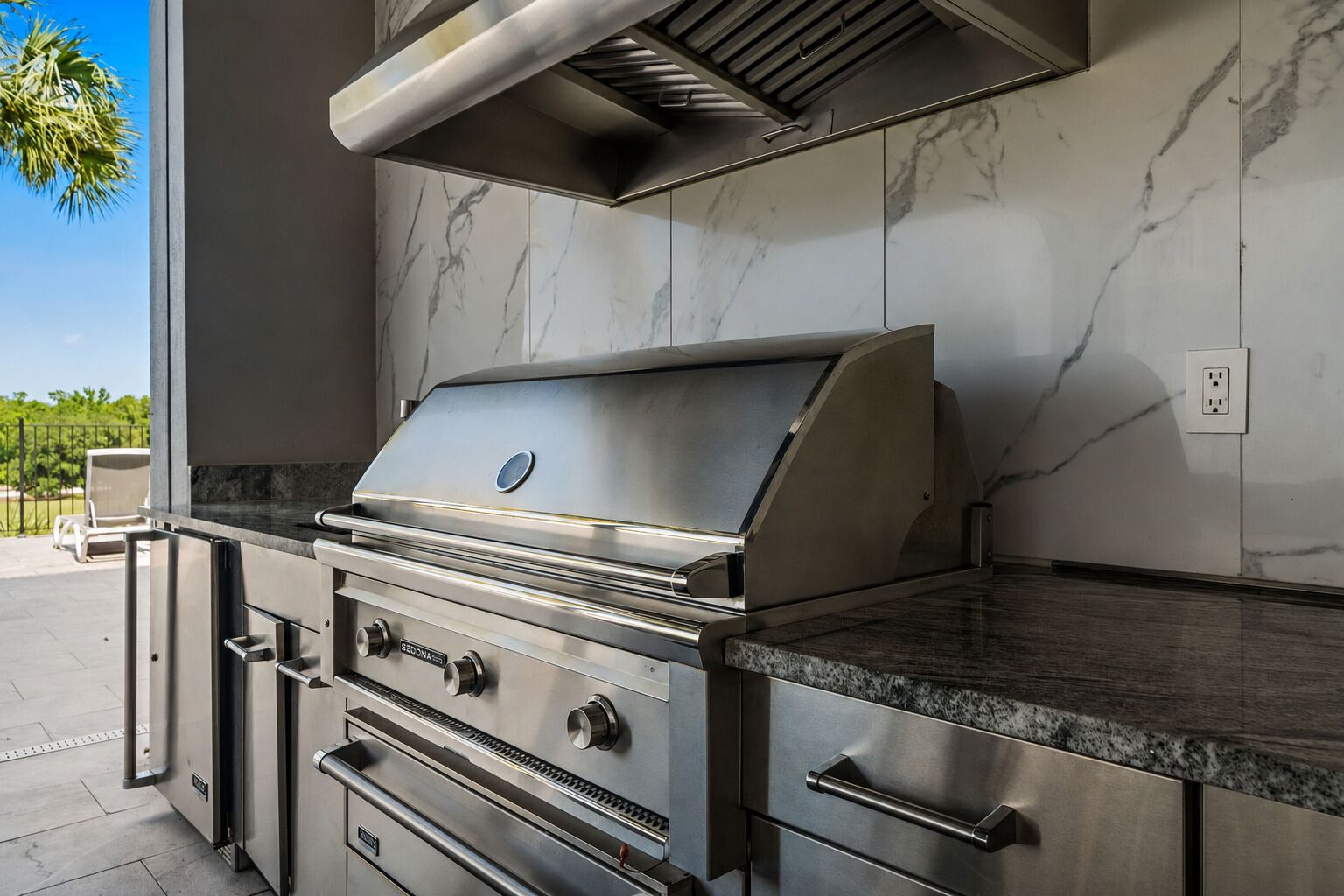 Cocina exterior de acero inoxidable con parrilla, cajones integrados y campana extractora.