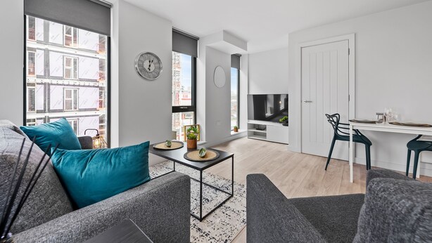 A modern living room with a sofa, a coffee table, and a dining area with a TV and table. - VICHY - Baltic Triangle Modern Apartment (Liverpool)