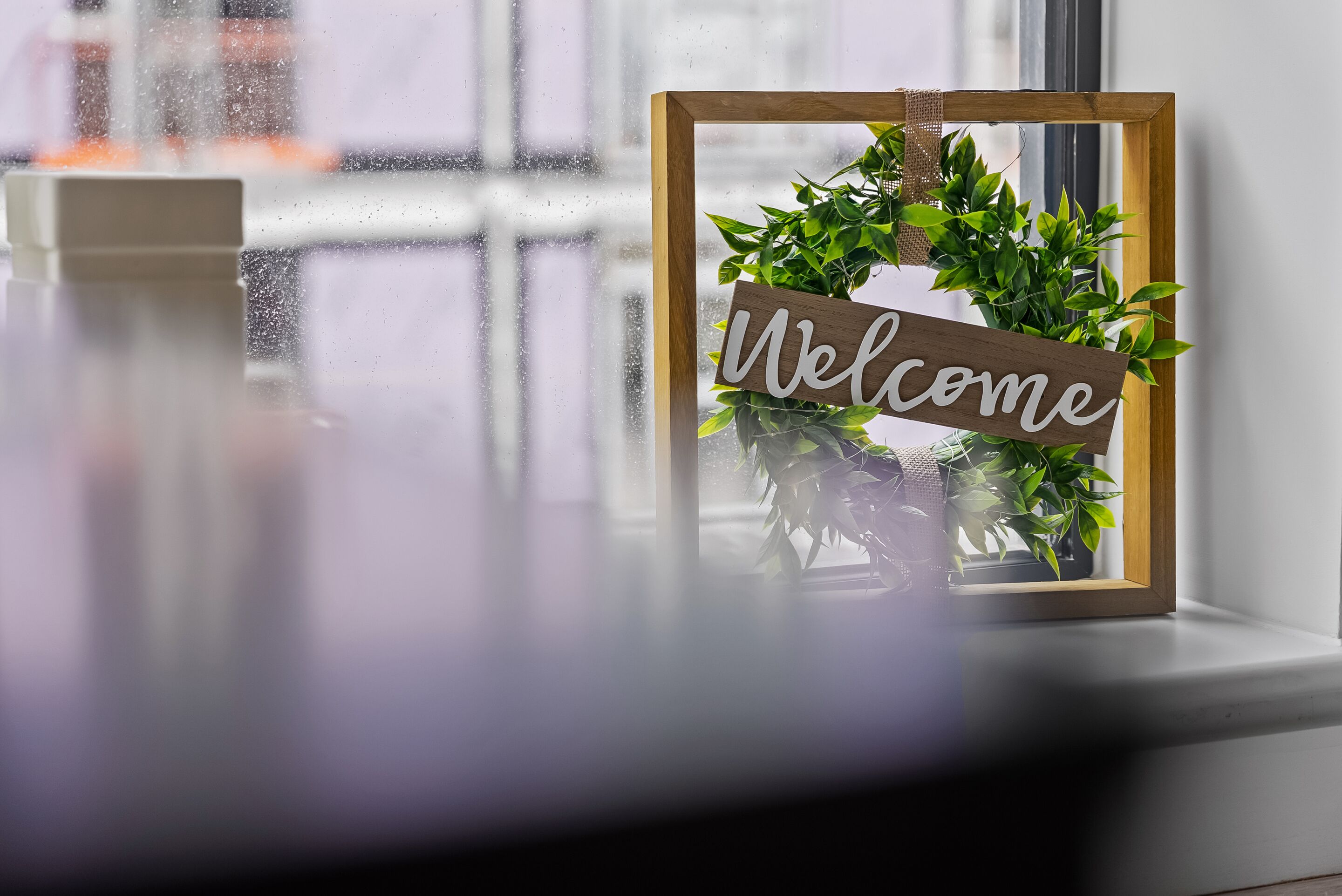A framed welcome sign with a wreath on a window sill.