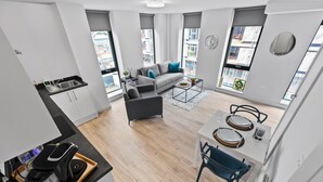 A modern apartment with a kitchen, dining area, and living room, featuring large windows and a city view. - VICHY - Baltic Triangle Modern Apartment (Liverpool)