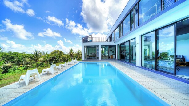 Una casa moderna con piscina, ventanas de cristal amplias y un balcón.