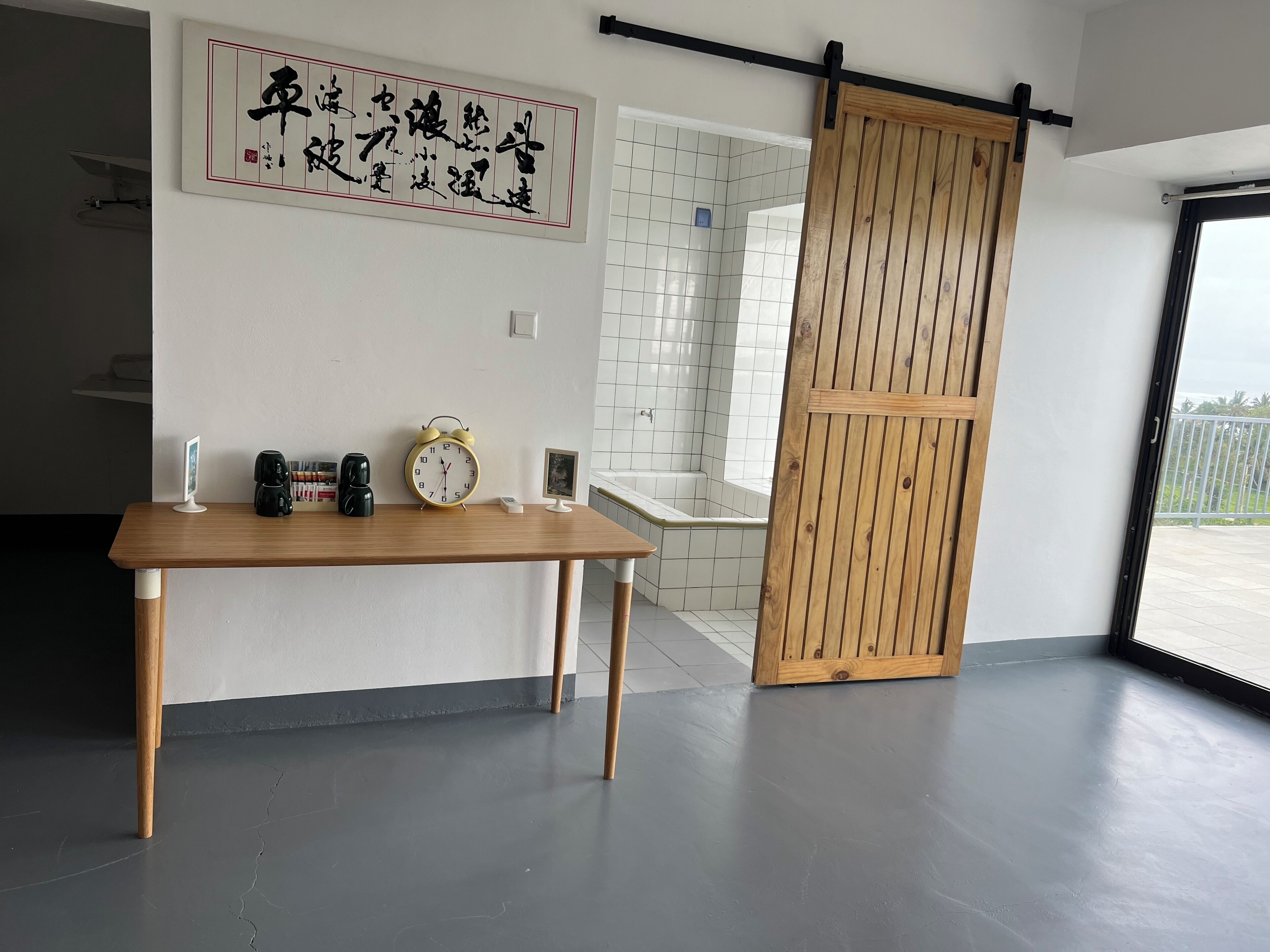 Un interior moderno con una mesa de madera, un reloj y una puerta corredera que da a un baño.