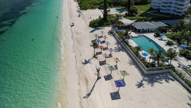 Un resort en la playa con piscina, sombrillas y un edificio grande al fondo.