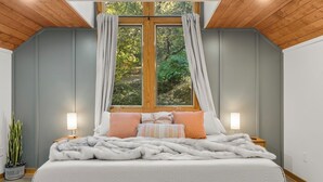 Une chambre avec un grand lit, deux lampes de chevet, une fenêtre avec des rideaux et un plafond en bois.