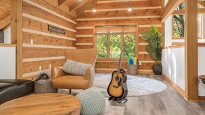 L’intérieur chaleureux d’un chalet en bois, avec un canapé en cuir, une guitare et une grande fenêtre donnant sur le paysage extérieur.