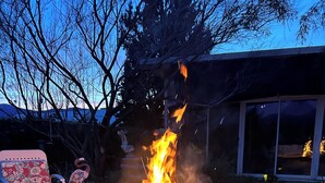 A fire in a pan outdoors with a chair and a building in the background.