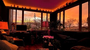 A cozy living room with a large window overlooking a scenic landscape, furnished with a sofa, coffee table, and a TV.