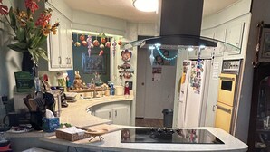 A kitchen with a central island, two bar stools, and various kitchen appliances.