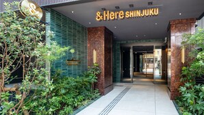 A modern building entrance with a neon sign reading "Hereshinjuku". - &Here SHINJUKU (Tokyo)
