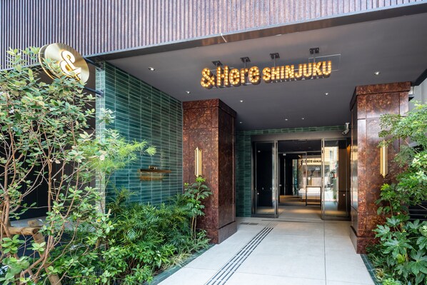 A modern building entrance with a neon sign reading "Hereshinjuku". - &Here SHINJUKU (Tokyo)