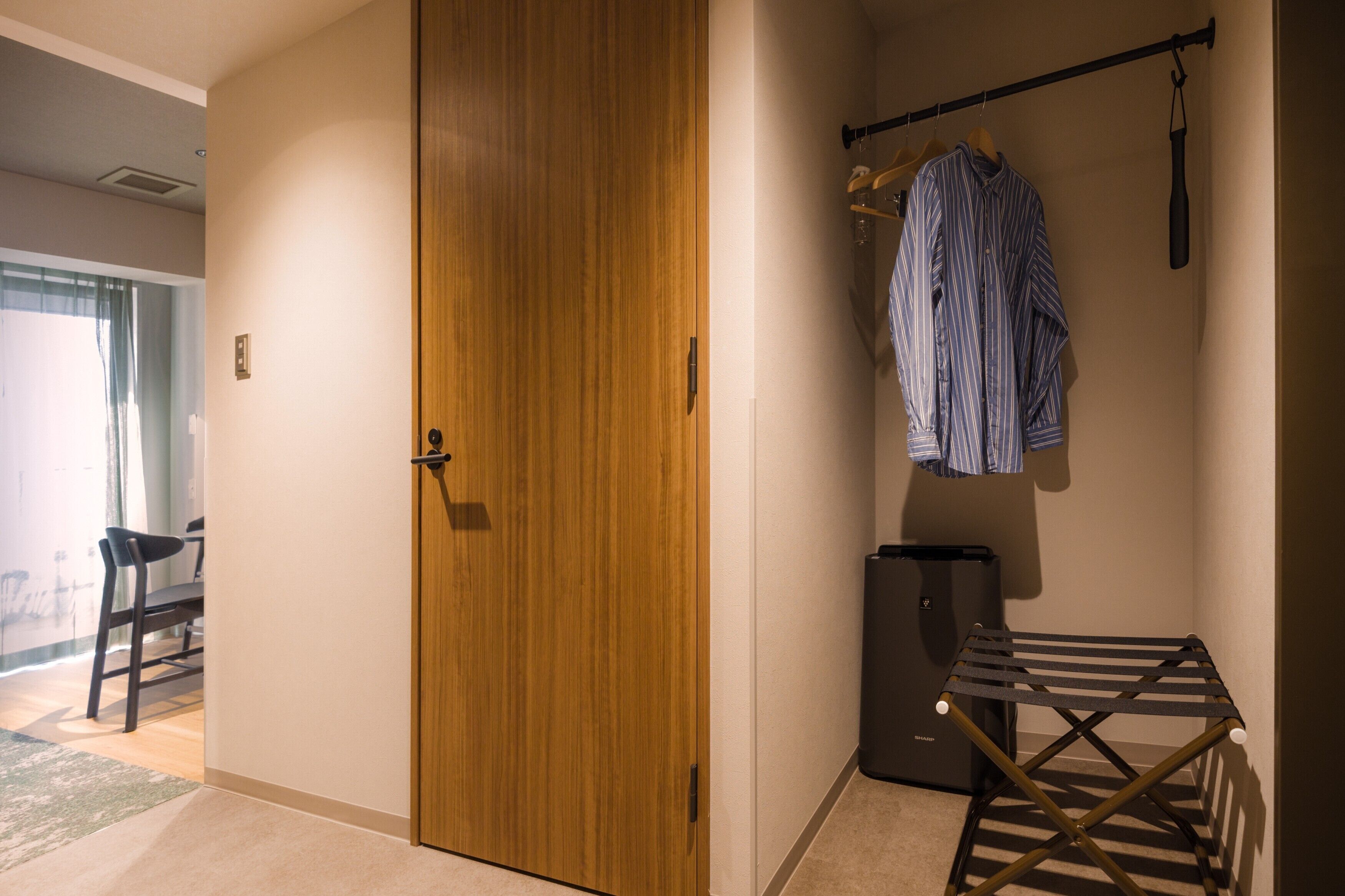 A room with a wooden door, a drying rack, a black trash bin, and a chair.