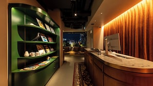 A modern reception area with a green curved bookshelf, a marble counter, and a view of the city at night. - &Here SHINJUKU (Tokyo)