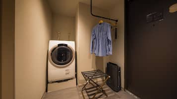 A laundry area with a washing machine, a drying rack, and a hanging rack with clothes.