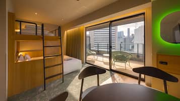 A modern hotel room with bunk beds, a balcony with a view of the city, and a dining area with chairs and a table.