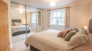 A bedroom with a large bed, a sliding door closet, and a window with curtains. - Modern 2-Bed Flat in Tavistock Centre (Tavistock)
