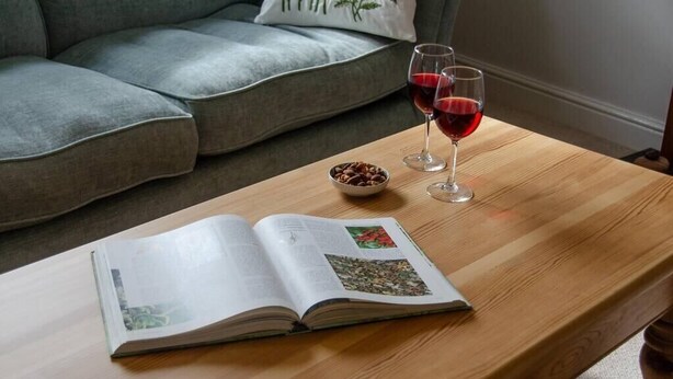 A book open on a wooden table with two glasses of red wine and a bowl of nuts. - Modern 2-Bed Flat in Tavistock Centre (Tavistock)