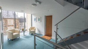 A modern interior with a staircase, two armchairs, a small table, and a view of the outside. - Modern 2-Bed Flat in Tavistock Centre (Tavistock)