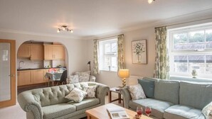 A cozy living room with a sofa, a coffee table with a book and glasses, and a dining area with a table and chairs. - Modern 2-Bed Flat in Tavistock Centre (Tavistock)