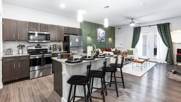A modern kitchen with stainless steel appliances, a central island with bar stools, and a dining area with a sofa and chairs. - Regal Hideaway | Pool Near Lackland + Med Ctr Gym! (San Antonio)
