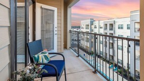A balcony with a chair and a view of adjacent buildings during sunset. - Regal Hideaway | Pool Near Lackland + Med Ctr Gym! (San Antonio)