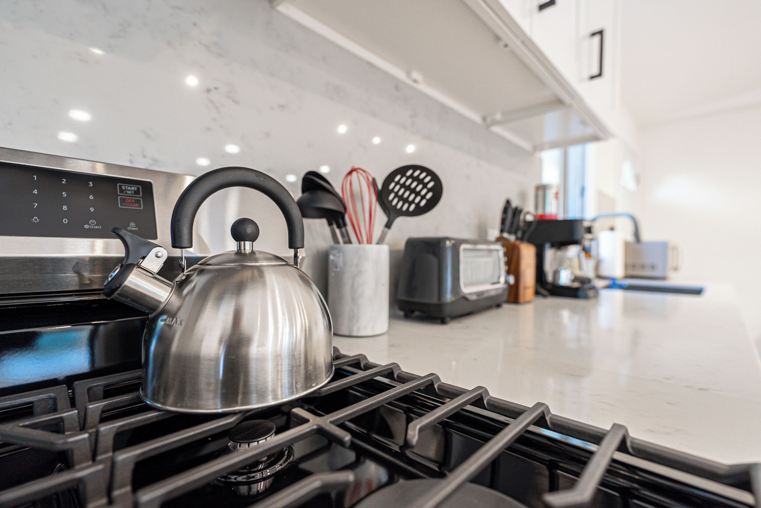Una cocina con estufa, hervidor y diferentes utensilios.