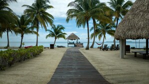 A wooden pathway leading to a beach with palm trees and a thatched-roof structure.