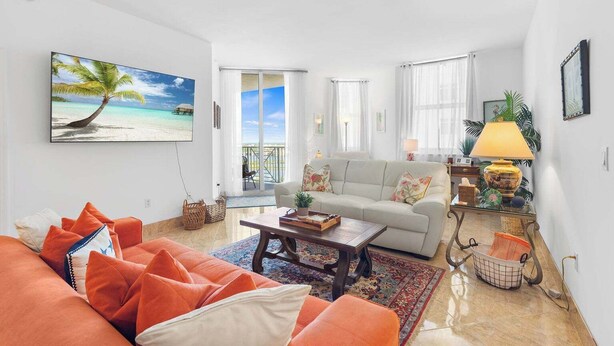 A living room with a sofa, a coffee table, and a painting of a beach scene. - Waterfront Downtown West Palm Beach with  Luxury Amenities (West Palm Beach)