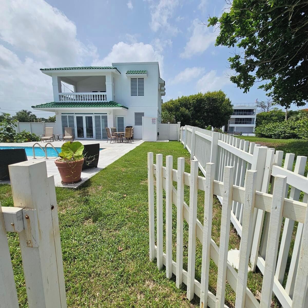 A white two-story house with a pool, a fenced backyard, and a patio with outdoor furniture.