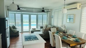 Uma cozinha moderna com ilha central, área de refeições com cadeiras brancas e vista para o oceano através de grandes janelas.