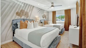 Una camera d'albergo moderna con un letto grande, un letto più piccolo, una scrivania e una ventola a soffitto.