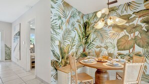 Zona pranzo con carta da parati a tema tropicale, arredamento in legno e un tavolo rotondo apparecchiato per quattro persone.