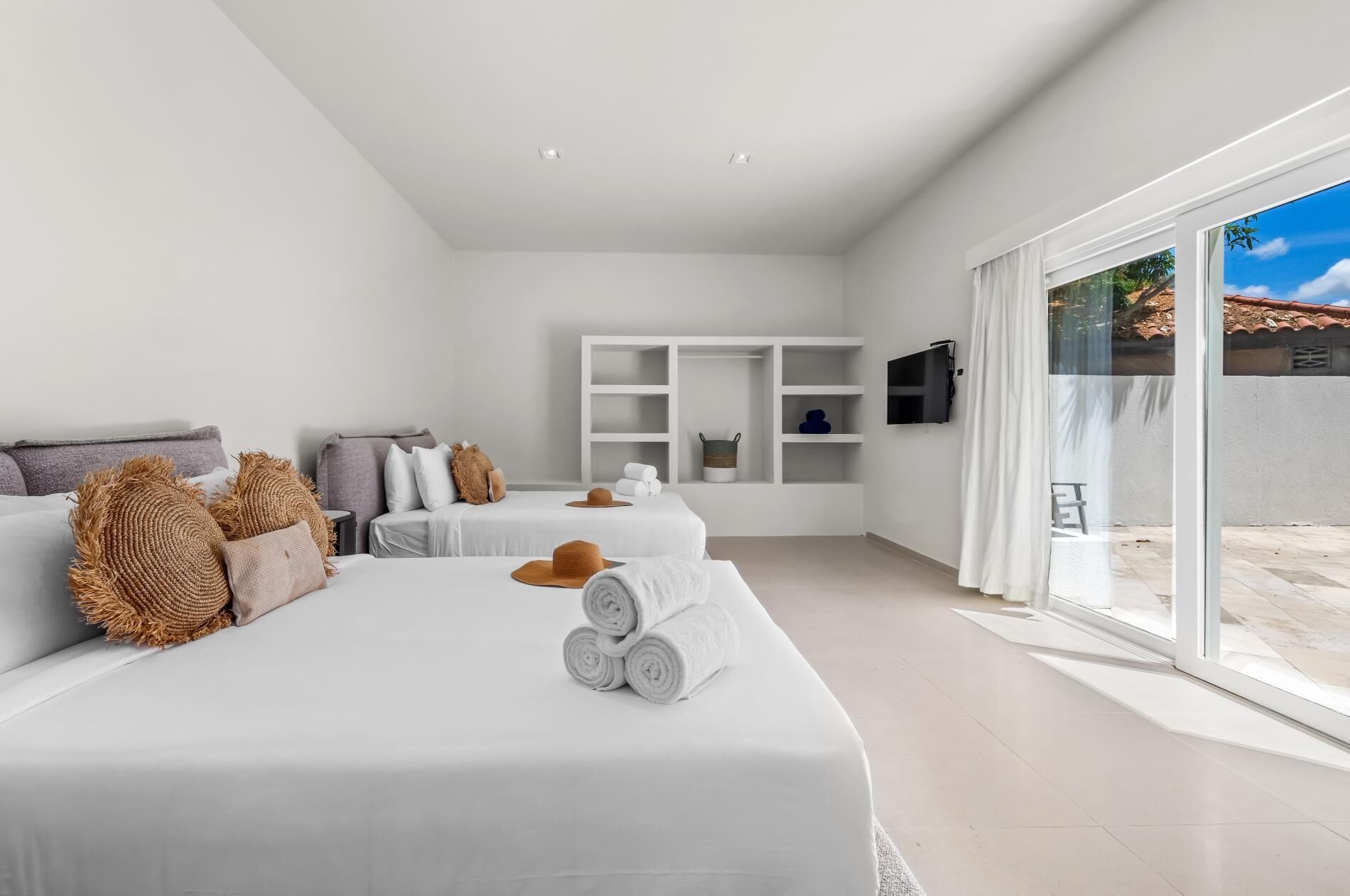 Een moderne hotelkamer met twee bedden, een televisie en een grote schuifglazen deur naar buiten.