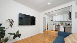 Una sala de estar moderna con un sofá azul, un televisor de pantalla plana montado en la pared y piso de madera.