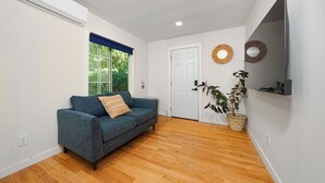 Una habitación con sofá azul, suelo de madera, televisor montado y planta en maceta.