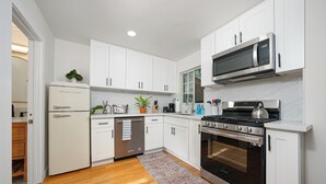 Una cocina moderna con armarios blancos, un refrigerador de acero inoxidable, un microondas, una estufa y un lavavajillas.