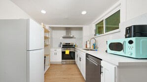 Una cocina moderna con armarios blancos, horno de acero inoxidable, lavavajillas y microondas color turquesa.
