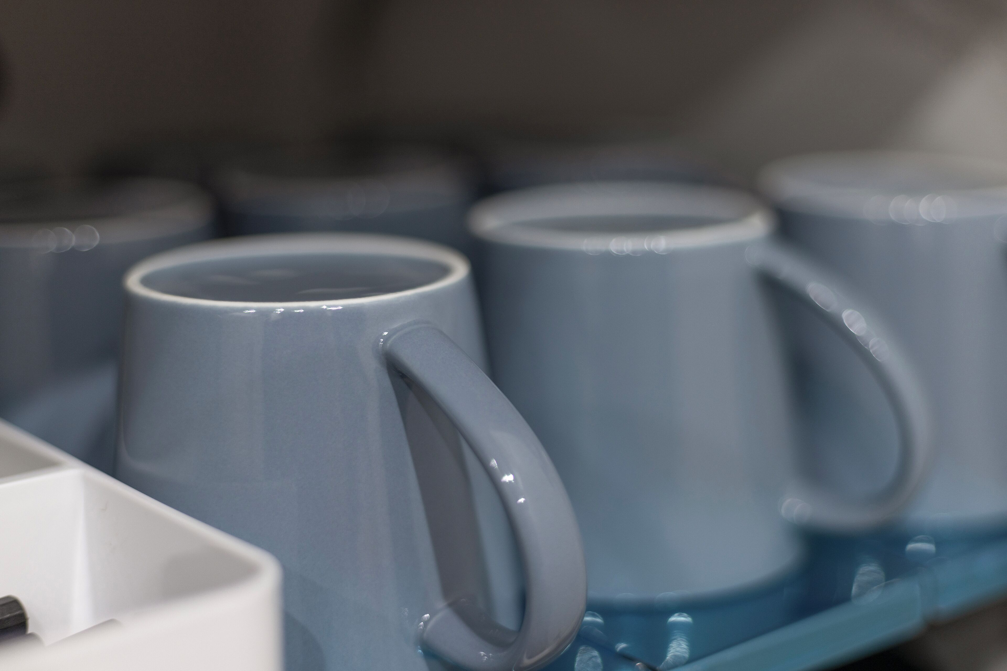 Primer plano de una hilera de tazas azules de cerámica con asa, dispuestas sobre una superficie azul.