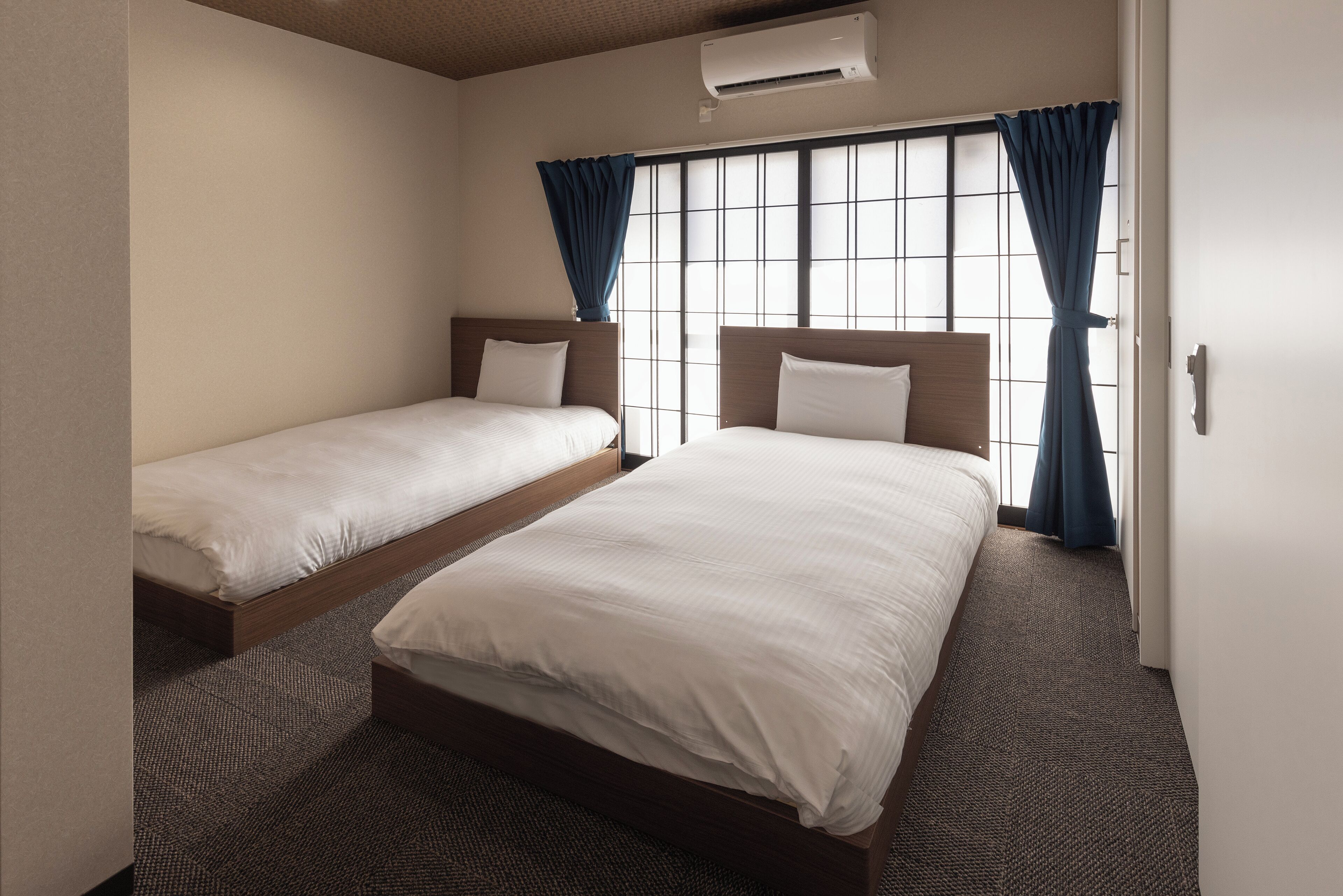 Ein Hotelzimmer mit zwei Einzelbetten, einem großen Fenster mit Vorhängen und einer Klimaanlage.